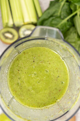 Making a green smoothie with celery, kiwi, apple and spinach in a blender, top view.