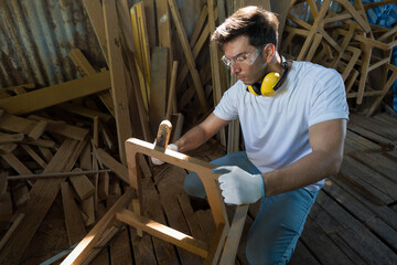 Young carpenter or woodworker with safety glasses, ear muff and protective gloves is sanding wood...