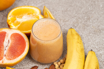 Fruit smoothie in a glass with banana, grapefruit and orange on grey background.