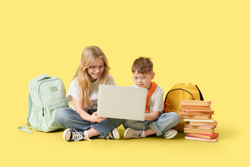 Cute little pupils in eyeglasses using laptop on yellow background
