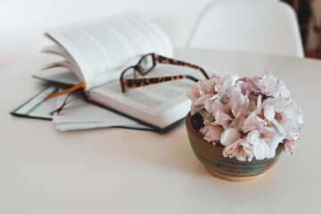 still life vase flowers, an open book, reading glasses, on white table
