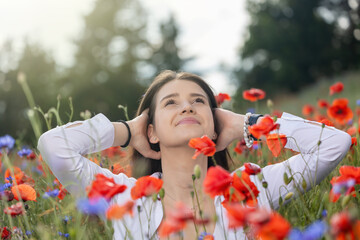 Beautiful brunette young woman is looking up at the sky posing in red poppies and blue cornflowers field.