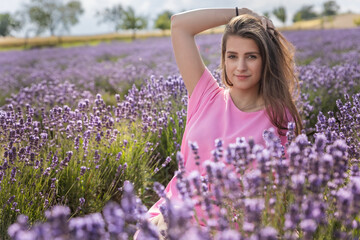Attractive girl is posing with hand in in her long hair in blooming lavender field. Horizontally.