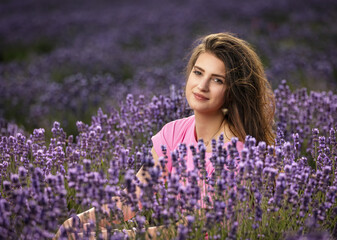 Atractive smiling long haired  
tanned girl is posing in a blooming lavender field. Horizontally. 