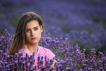 Cool brunette long haired  tanned girl is posing in a lavender field. Horizontally. 