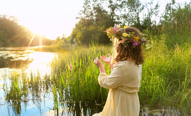 girl in flower wreath stand in river. summer nature background. Floral crown, symbol of summer...
