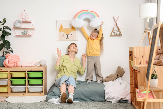 Nanny and little girl with rainbow pillow in bedroom