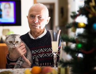 Older man with gray cat sitting at home table at Christmas - 807811188