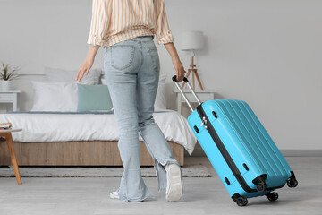 Woman with suitcase in light hotel room, back view