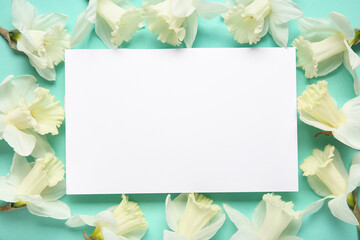 Frame made of daffodil flowers and blank card on turquoise background. Top view