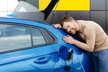 New car owner. Happy man touching hugging his new auto cherfully buying vehicle in auto dealership.