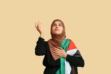 Young Muslim woman with Palestine flag praying on beige background. Sorrow concept