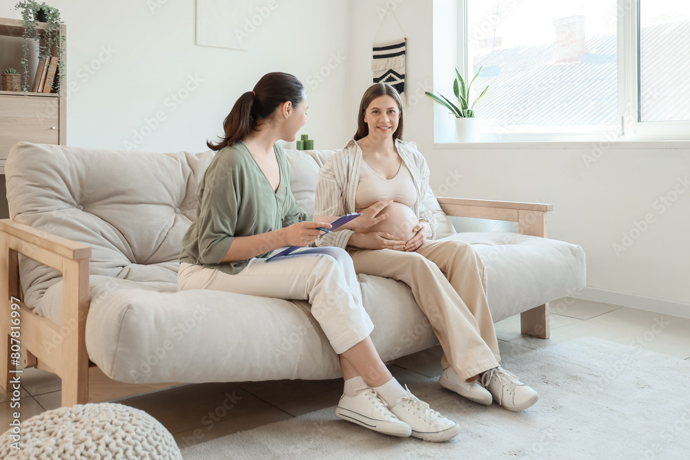 Sticker doula with clipboard and pregnant woman sitting on sofa at home