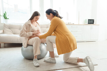 Young pregnant woman sitting on fitball with doula at home