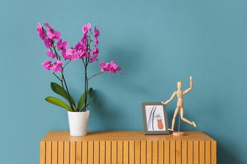 Orchid flower with frame and mannequin on commode near blue wall