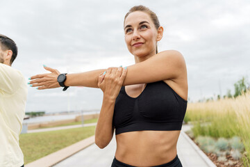 Close-up of an active Caucasian woman stretching her arm, wearing a black sports bra, smartwatch,...