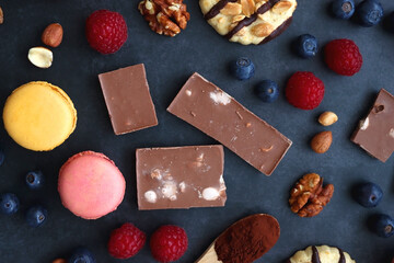 Macarons, chocolate, cookies, berries and various nuts on dark blue background. Top view.