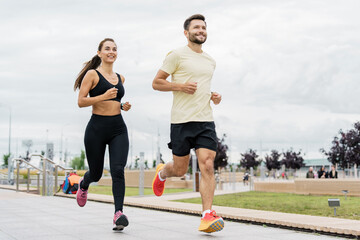 An energetic couple in athletic attire happily running along a city park pathway, with a vibrant...