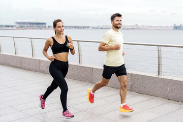 A spirited couple running along a seaside promenade, the woman leading with focus and the man...