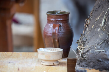 Ceramic jug, bowl with flour and medieval clay oven for baking bread close-up, dishes on a wooden table, medieval lifestyle, still life