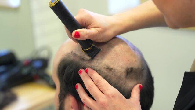 Hairdresser shaving the head of a bald man to attach a new wig