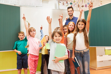 Schoolkids raising hands in classroom
