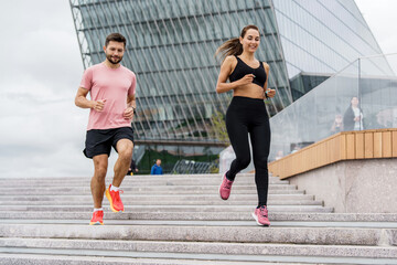 An athletic couple energetically runs up a set of stairs in a modern urban landscape, showcasing...