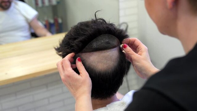 Top view close-up of a hairstylist attaching a wig to a man using adhesive stripes