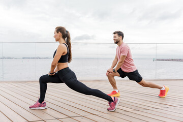A focused couple performs synchronized lunges on a seaside promenade, wearing athletic gear and...