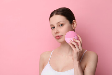 Washing face. Young woman with cleansing brush on pink background, space for text