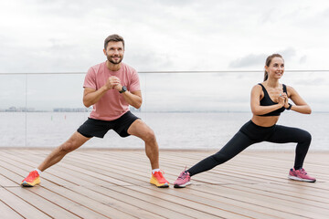 A vibrant couple engage in side lunges on a seaside promenade, each showing determination while...