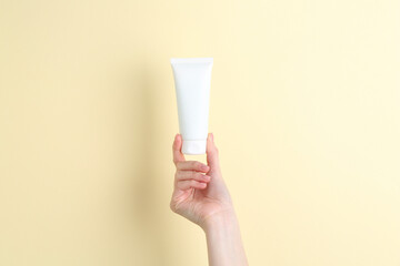 Woman holding tube of cream on yellow background, closeup