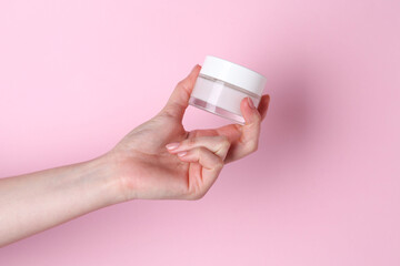 Woman holding jar of cream on pink background, closeup