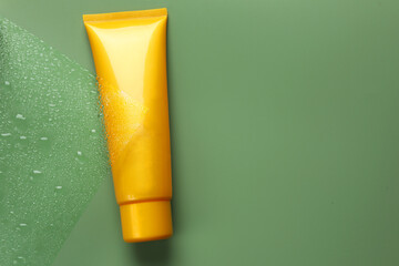 Tube with moisturizing cream on wet green surface, top view. Space for text