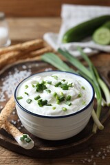 Delicious yogurt, green onion, grissini and salt on wooden table, closeup