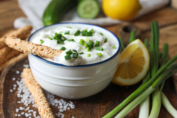 Delicious yogurt, green onion, grissini and lemon on table, closeup
