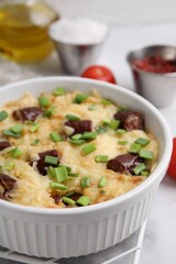 Tasty sausage casserole with green onion in baking dish on white table, closeup