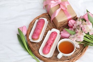 Tasty breakfast. Delicious eclairs, tea, flowers and gift box on bed