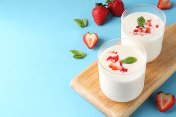 Tasty yogurt in glasses and strawberries on light blue wooden table. Space for text
