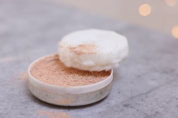 Face powder and puff applicator on grey textured table, closeup