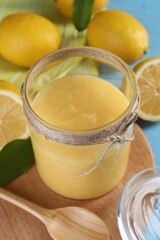 Delicious lemon curd in glass jar, fresh citrus fruits, spoon and green leaves on table, closeup