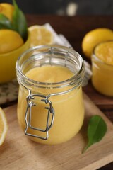 Delicious lemon curd in glass jar and fresh citrus fruit on table