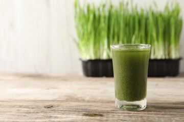 Wheat grass drink in shot glass on wooden table, closeup. Space for text