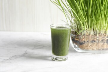 Wheat grass drink in shot glass and fresh sprouts on white marble table