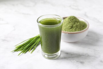 Wheat grass drink in shot glass on white marble table, closeup