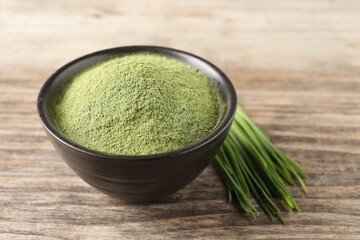 Wheat grass powder in bowl and fresh sprouts on wooden table, closeup