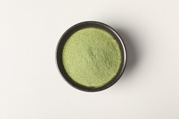 Wheat grass powder in bowl on light table, top view