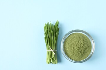Wheat grass powder in glass bowl and fresh sprouts on light blue table, flat lay. Space for text