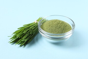 Wheat grass powder in glass bowl and fresh sprouts on light blue table