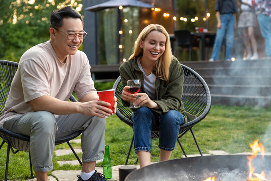 Diverse friends sitting together on backyard with drinks enjoying weekend party - Powered by Adobe